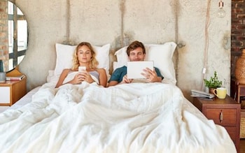 Young couple using digital tablet and mobile phone in bed
